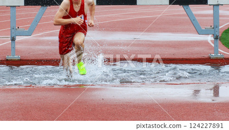 Runner Splashes Through Water Obstacle on Track During a Steeplechase Race Runner Splashes Through Water Obstacle on Track During a Steeplechase Race 124227891