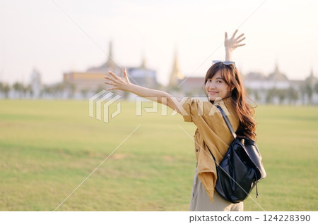 A Traveler Asian woman in 30s, bathed in golden glow of a Bangkok sunset, laughs with carefree joy, her arms outstretched as if to embrace freedom of the moment. Backpack strapped on. A Traveler Asian woman in 30s, bathed in golden glow of a Bangkok sunset, laughs with carefree joy, her arms outstretched as if to embrace freedom of the moment. Backpack strapped on. 124228390