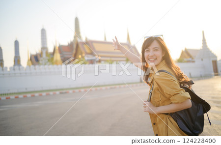 Traveler asian woman in her 30s, backpack slung over her shoulder, explores the intricate details of Wat Pra Kaew with childlike wonder. Sunlight dances on the golden rooftops. 124228400