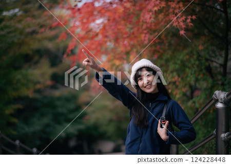 Asian woman in casual dress embraces the beauty of fall in Kyoto, enjoying a holiday filled with friends, smiles, and colorful foliage by the lake. A cheerful and scenic journey. 124228448