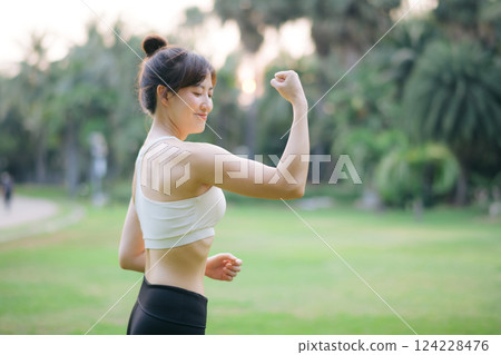 Strong fitness asian woman runner showing off muscular arms flexing biceps. wellbeing success concept. Strong fitness asian woman runner showing off muscular arms flexing biceps. wellbeing success concept. 124228476