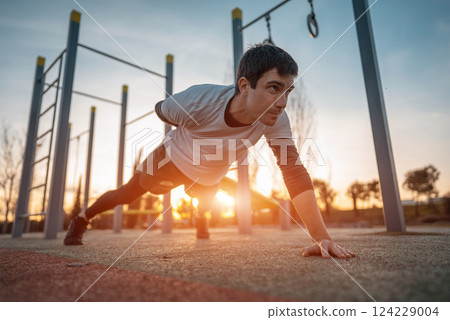 young athletic man exercising at fitness calisthenics workout and standing plank at street gym during sunset, body improvement and strength training concept 124229004