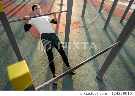 young athletic man exercising at fitness calisthenics workout and do australian pull-ups or inverted rows at street gym during sunset, body improvement and strength training concept 124229010