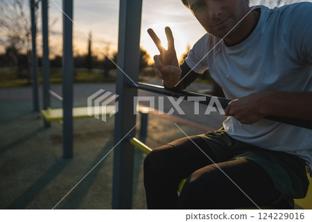 cheerful athletic man resting after exercising abs bench crunch at fitness calisthenics workout at street gym during sunset, relax after body improvement and strength training concept 124229016
