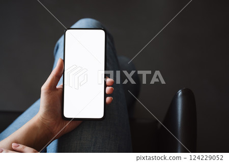 Young woman hold smarphone with white screen while sitting in a chair Young woman hold smarphone with white screen while sitting in a chair 124229052