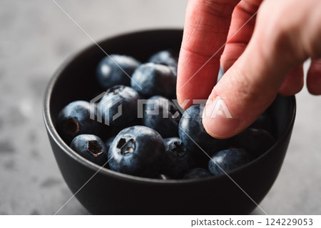 Man hand pick ripe blueberries from black bowl on concrete background closeup Man hand pick ripe blueberries from black bowl on concrete background closeup 124229053