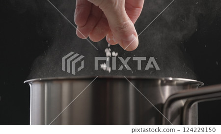 man salting boiling water in saucepan man salting boiling water in saucepan 124229150