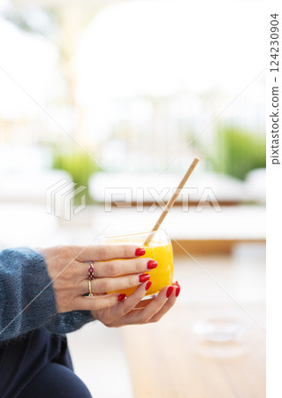 Close-up hands of woman holding glass of fresh orange juice, refreshing citrus drink for healthy lifestyle, minimalistic composition with vibrant blue and orange color and summer vibes Close-up hands of woman holding glass of fresh orange juice, refreshing citrus drink for healthy lifestyle, minimalistic composition with vibrant blue and orange color and summer vibes 124230904