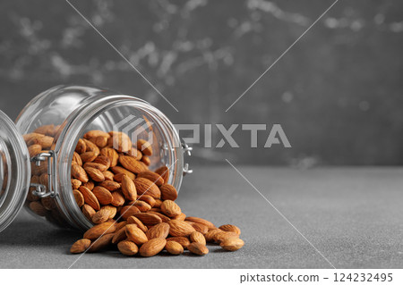 Shelled almonds spilling from glass jar onto gray surface, creating visually appealing arrangement with potential use in healthy food and lifestyle contexts 124232495