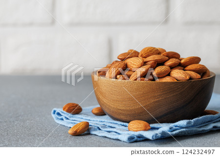 Wooden bowl full of raw almonds sits on gray table with blue napkin, creating warm and inviting scene promoting healthy eating and snacking Wooden bowl full of raw almonds sits on gray table with blue napkin, creating warm and inviting scene promoting healthy eating and snacking 124232497