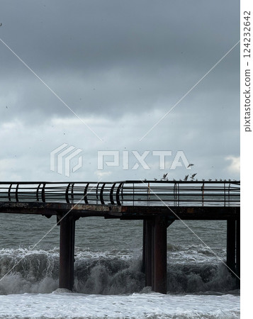 Old pier with crashing waves and flying birds in stormy weather 124232642