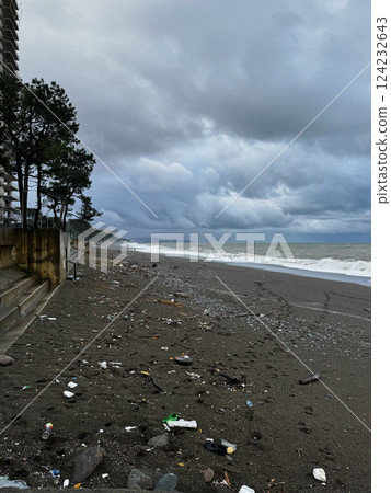 Polluted black sand beach with ocean waves under a stormy sky 124232643