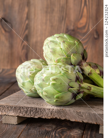 Fresh raw artichokes on vintage cutting board with rustic wooden background texture 124232824