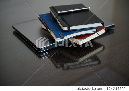 Stacked Notebooks and Laptop on a Reflective Wooden Desk Stacked Notebooks and Laptop on a Reflective Wooden Desk 124233221