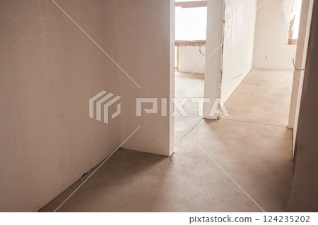 The room is under construction with a rough finish, plastered walls, concrete floor. Wiring of ventilation pipes on a concrete ceiling in a house under construction. The room is under construction with a rough finish, plastered walls, concrete floor. Wiring of ventilation pipes on a concrete ceiling in a house under construction. 124235202