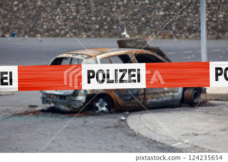 German police tape in front of a burnt-out car 124235654
