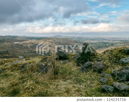 Rural setting. Large gray rocks dominate a hilltop. Fields and distant horizon under cloudy skies. Rural setting. Large gray rocks dominate a hilltop. Fields and distant horizon under cloudy skies. 124235716