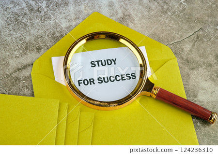 A magnifying glass focuses on the text study for success placed on a white paper inside a vibrant yellow envelope, indicating educational aspirations 124236310