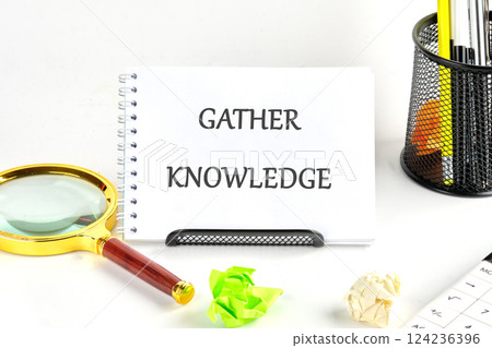Workspace emphasizes the theme of gathering knowledge with a notebook, magnifying glass, and creative tools for learning enhancement 124236396
