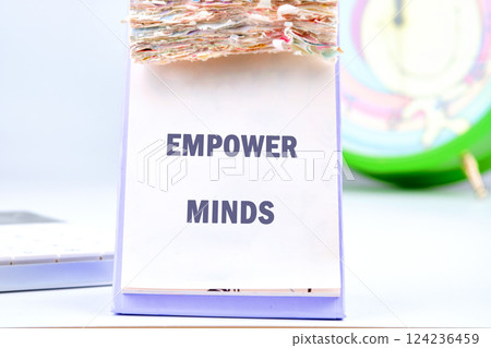 A notepad displaying the words empower minds is placed on a desk alongside a clock and materials related to business and finance, emphasizing educational advancement 124236459
