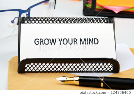 A desk setup showcases a sign that promotes personal and professional growth in business and finance education, accompanied by office supplies and glasses 124236460