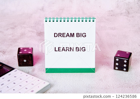 A notepad with the words Dream Big Learn Big is surrounded by dice and a calculator, symbolizing risk and strategy in business education A notepad with the words Dream Big Learn Big is surrounded by dice and a calculator, symbolizing risk and strategy in business education 124236586