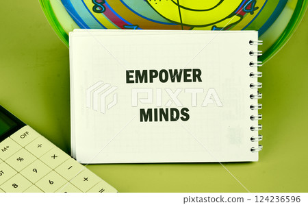 A white notebook open to the phrase Empower Minds is placed next to a calculator and a colorful circular chart, symbolizing business and finance education 124236596