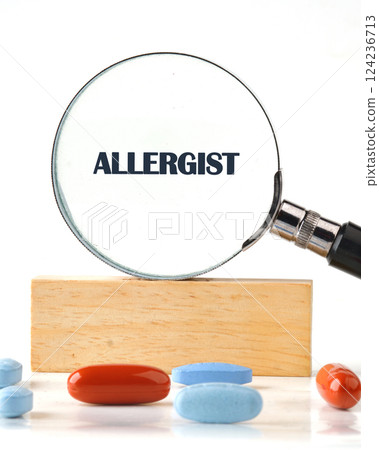 A magnifying glass highlights the word allergist, showcasing important allergy medications on a table 124236713