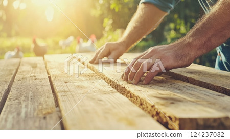 Farmer focuses on woodworking to build a chicken coop while free-range chickens roam nearby 124237082