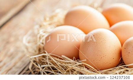 Close-up of freshly laid eggs in a straw nest, highlighting details and warm tones 124237108