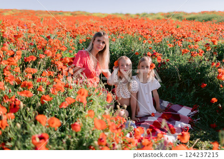 Happy family: mother with daughters in a blooming poppy field. Beauty smiling woman and kids in dress with red flowers Happy family: mother with daughters in a blooming poppy field. Beauty smiling woman and kids in dress with red flowers 124237215
