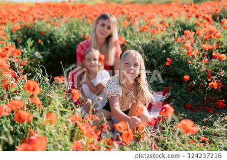 Happy family: mother with daughters in a blooming poppy field. Beauty smiling woman and kids in dress with red flowers Happy family: mother with daughters in a blooming poppy field. Beauty smiling woman and kids in dress with red flowers 124237216