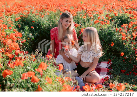 Happy family: mother with daughters in a blooming poppy field. Beauty smiling woman and kids in dress with red flowers 124237217