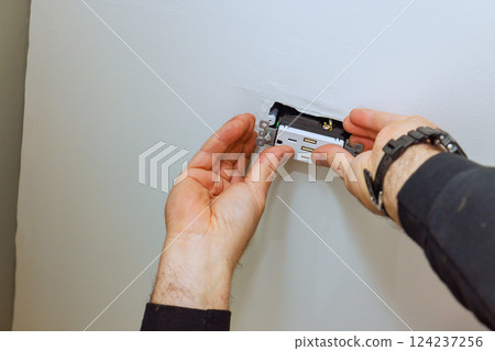 Electrician person is carefully placing an electrical outlet into ceiling of home installation 124237256