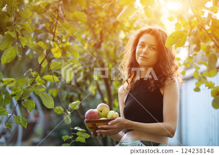 smiling female with apples in bowl in sunny garden, concept of gathering harvest 124238148