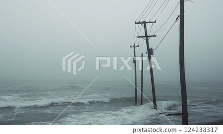 Misty coastal scene with broken wooden poles and a damaged power line standing in rough ocean waves. 124238317