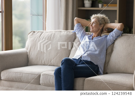 Carefree older woman sitting on cozy sofa with dreamy smile 124239548