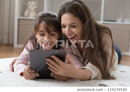 Happy young mom little daughter lying on carpet using tablet Happy young mom little daughter lying on carpet using tablet 124239580