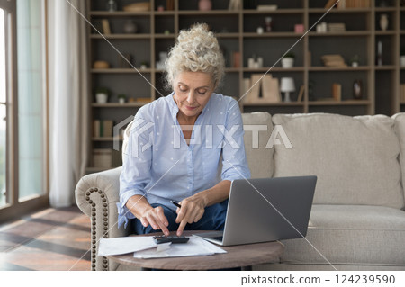 Woman pensioner engaged in finance paperwork at cozy home office 124239590