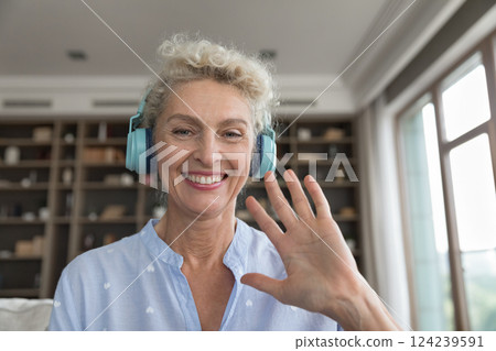 Mature woman in headphones looking at web camera waving hand 124239591