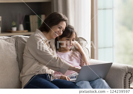 Friendly young mom little daughter sitting on couch with notebook Friendly young mom little daughter sitting on couch with notebook 124239597