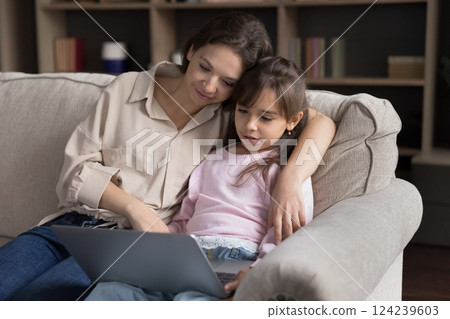 Little girl with loving young mum using notebook on couch 124239603