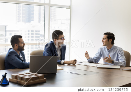 Three professionals engaged in discussion seated at conference table 124239755