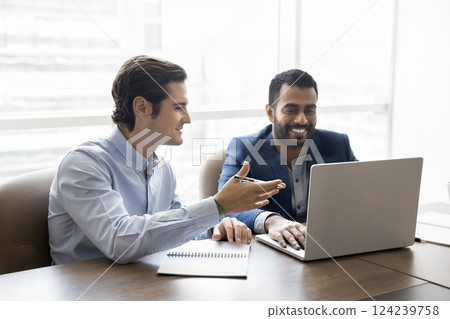 Teammates working on joint project seated at desk using laptop Teammates working on joint project seated at desk using laptop 124239758