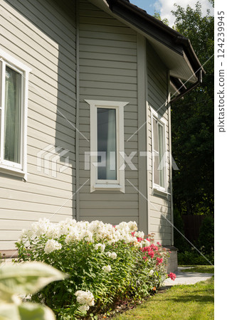 Contemporary gray two-story house of timber with bay window in countryside in summer. House have nice landscaping and flowers. Russian dacha in Moscow region. Contemporary gray two-story house of timber with bay window in countryside in summer. House have nice landscaping and flowers. Russian dacha in Moscow region. 124239945