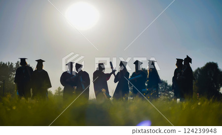 Silhouetted graduates holding diplomas, celebrating their academic achievement at a sunset graduation ceremony, marking a significant milestone 124239948