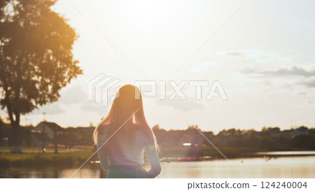 Blonde teenager savoring golden sunset reflecting on serene lake waters, soft suburban landscape surrounding her peaceful moment 124240004