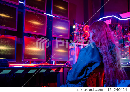 Asian woman holding laptop computer with CCTV room she check maintain security in monitor display, Hacker wearing a black jacket and has long red hair with multiple computer monitors 124240424