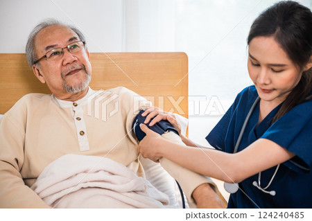 Asian caring nurse attentively checking blood pressure on a patient senior old man in their hospital bed visit from medical nurse monitoring heart with sphygmomanometer, medical healthcare Asian caring nurse attentively checking blood pressure on a patient senior old man in their hospital bed visit from medical nurse monitoring heart with sphygmomanometer, medical healthcare 124240485