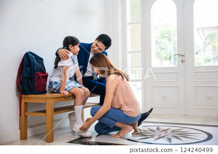 Family Asian mother helping her primary daughter put shoes and get dressed in front of home before go to school, with the father dressed in a suit sitting and waiting to be dropped off Family Asian mother helping her primary daughter put shoes and get dressed in front of home before go to school, with the father dressed in a suit sitting and waiting to be dropped off 124240499
